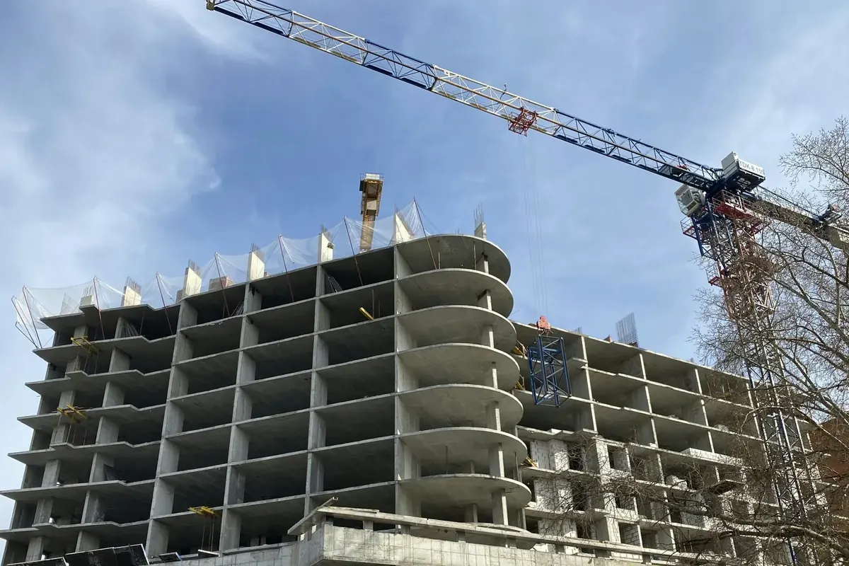 Guindaste sobre a estrutura de concreto de um edifício residencial em construção, sob céu azul
